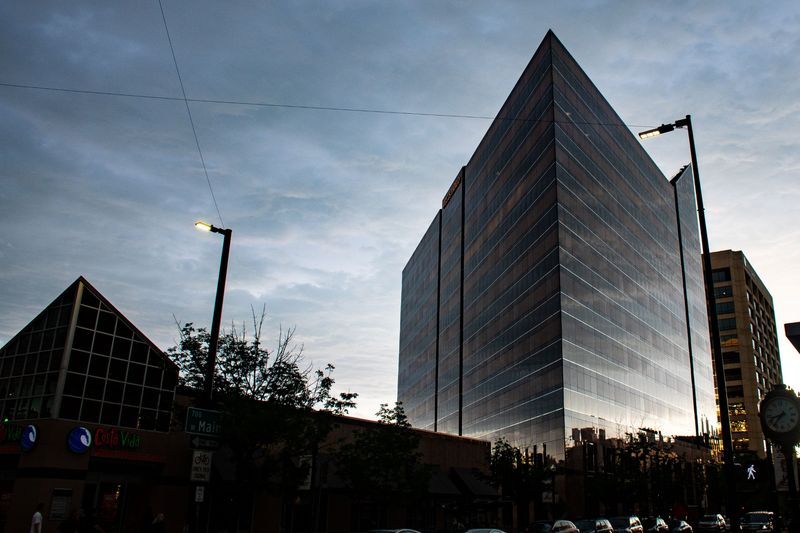 Skyscraper with pyramid-shaped structure and street lights against a cloudy sky.