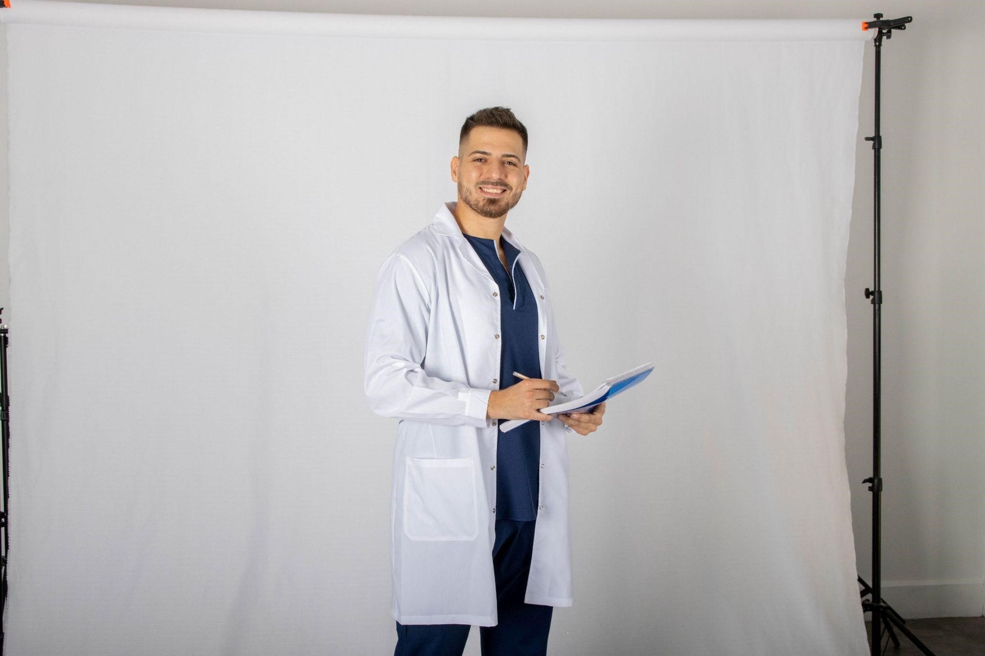 Un médico está de pie frente a un fondo blanco sosteniendo un portapapeles.