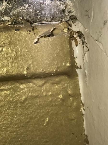 Gold painted textured wall corner with damaged paint and cobwebs.