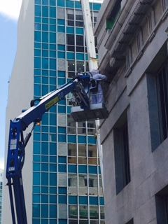 A blue lift raises a worker toward a building facade. The worker is inspecting the stone exterior.