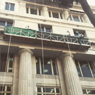 Workers on a suspended scaffold cleaning a tall, ornate building with large columns.