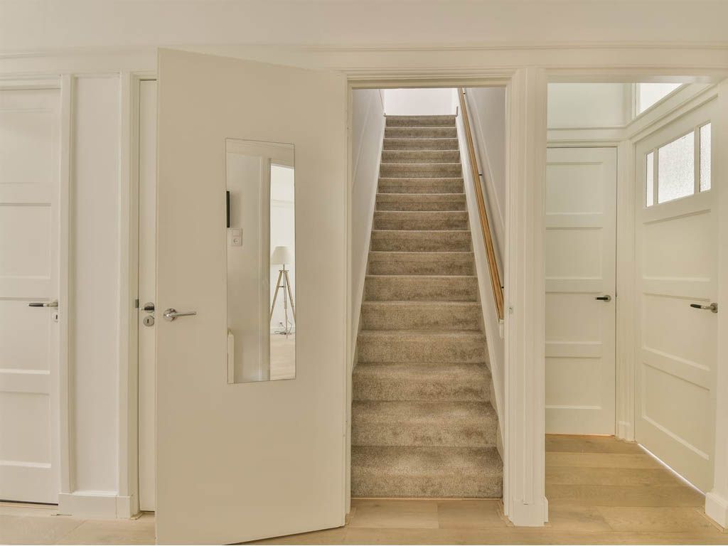 Hallway with stairs and white doors; carpeted stairs lead up, two doors on either side, one with a glass panel.