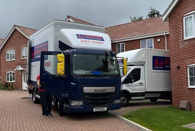 Two AJ Stephenson Removal trucks are parked in front of a brick building.