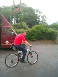 A man is riding a bike down a road next to a red van.