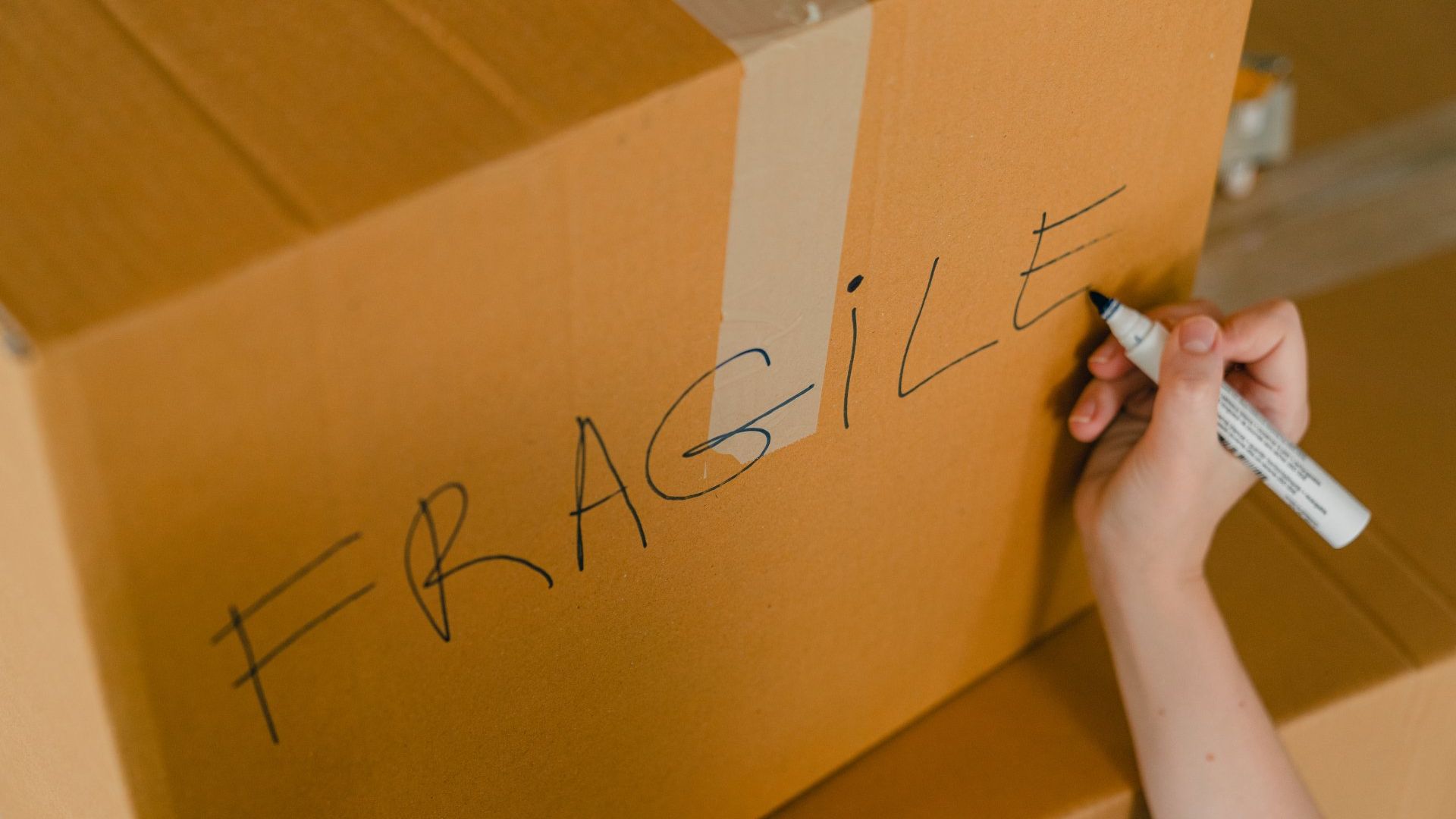 A person is writing fragile on a cardboard box with a marker.