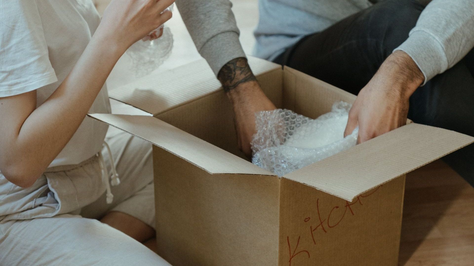 A man and a woman are sitting on the floor packing away belongings in a cardboard box.