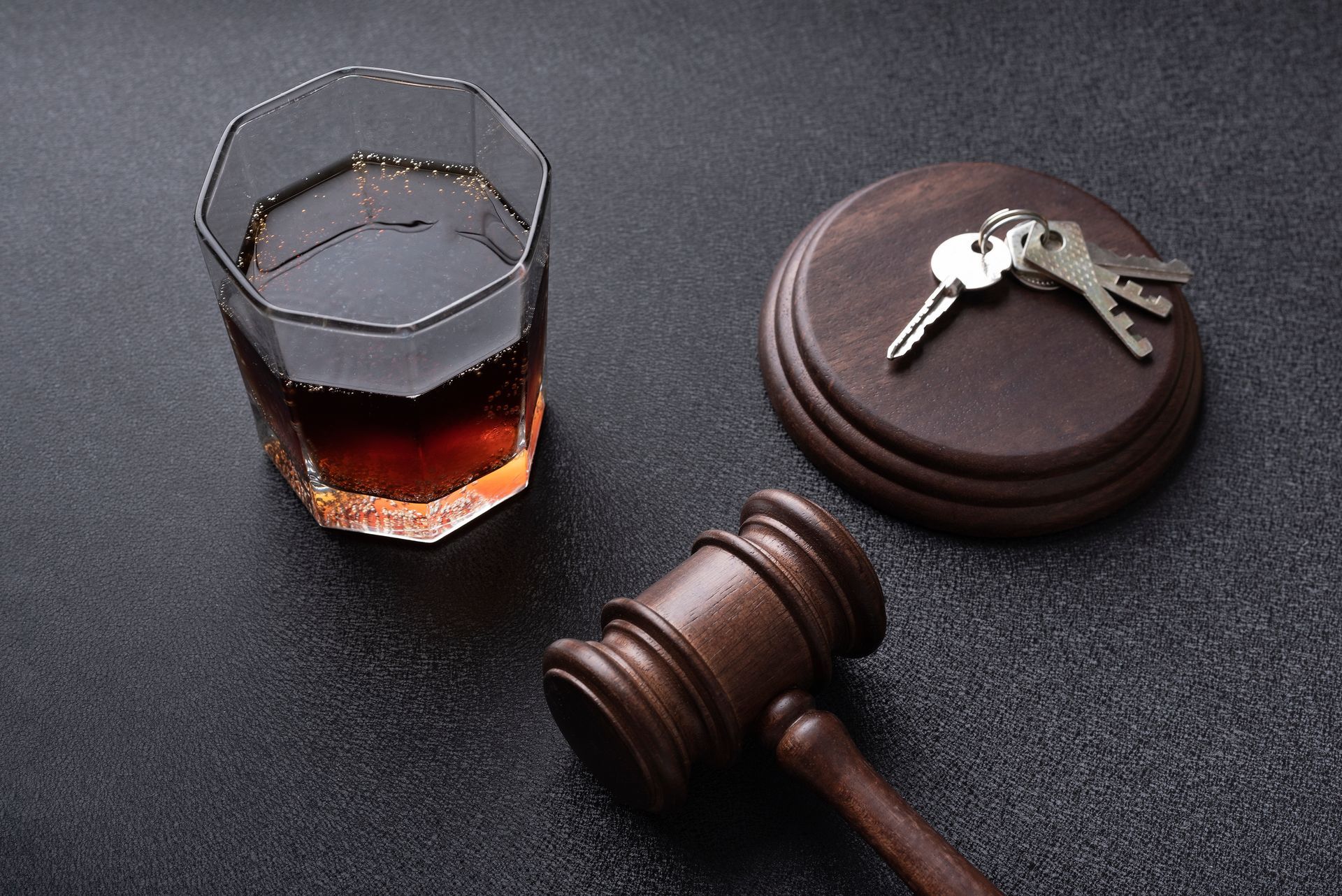 A glass of liquor, car keys, and a gavel suggest legal risks of drinking and driving.