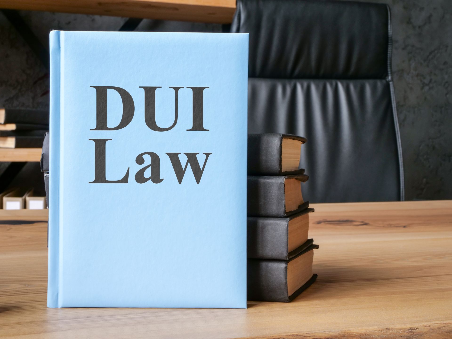 Blue book titled DUI Law on desk beside stacked legal books and office chair.