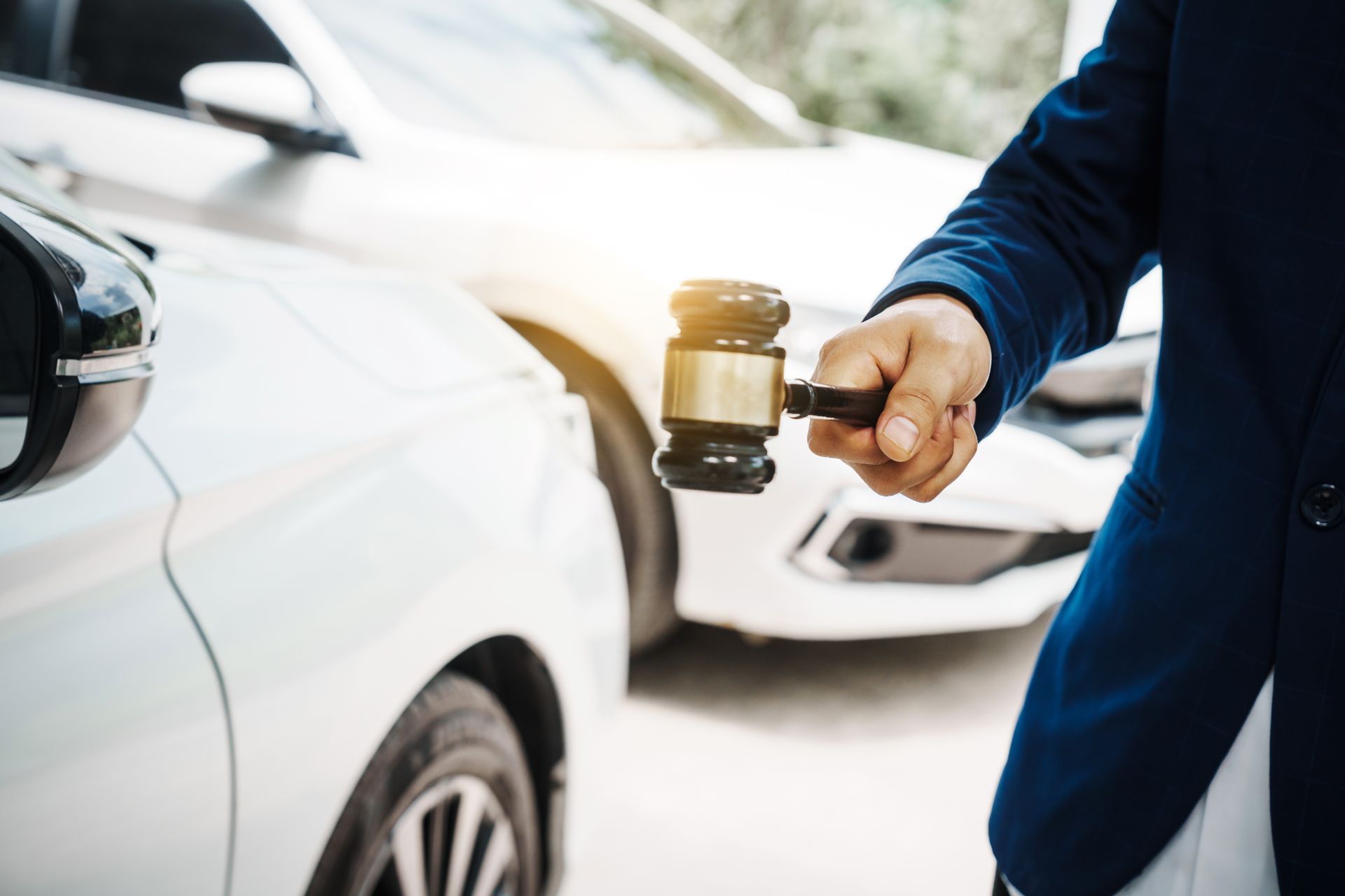 A man wearing a suit walks towards a white car while holding a gavel. A man wearing a suit walks towards a white car while holding a gavel.
