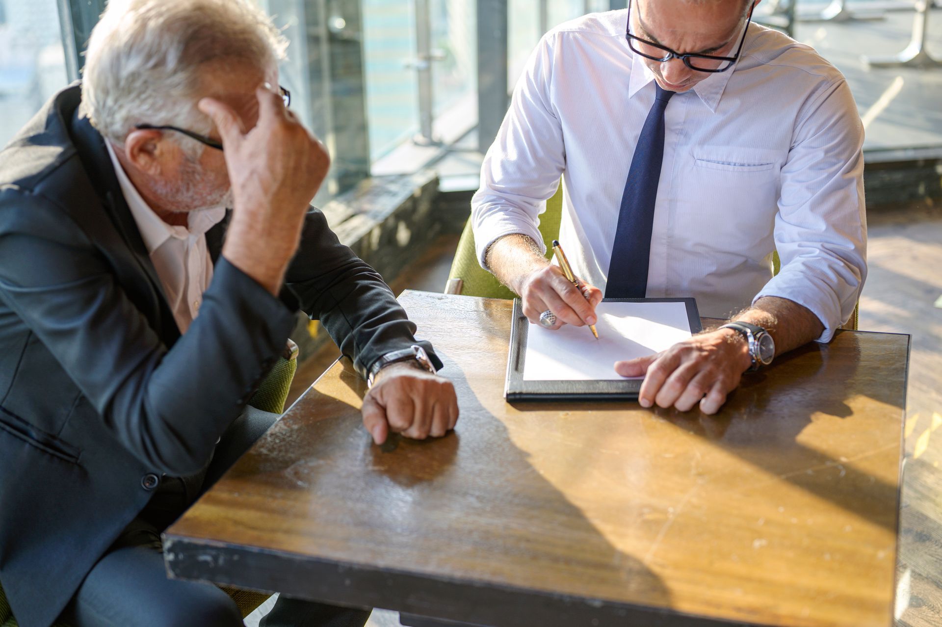 A DUI defense lawyer educates a worried client while writing on documents sitting on a wooden table.