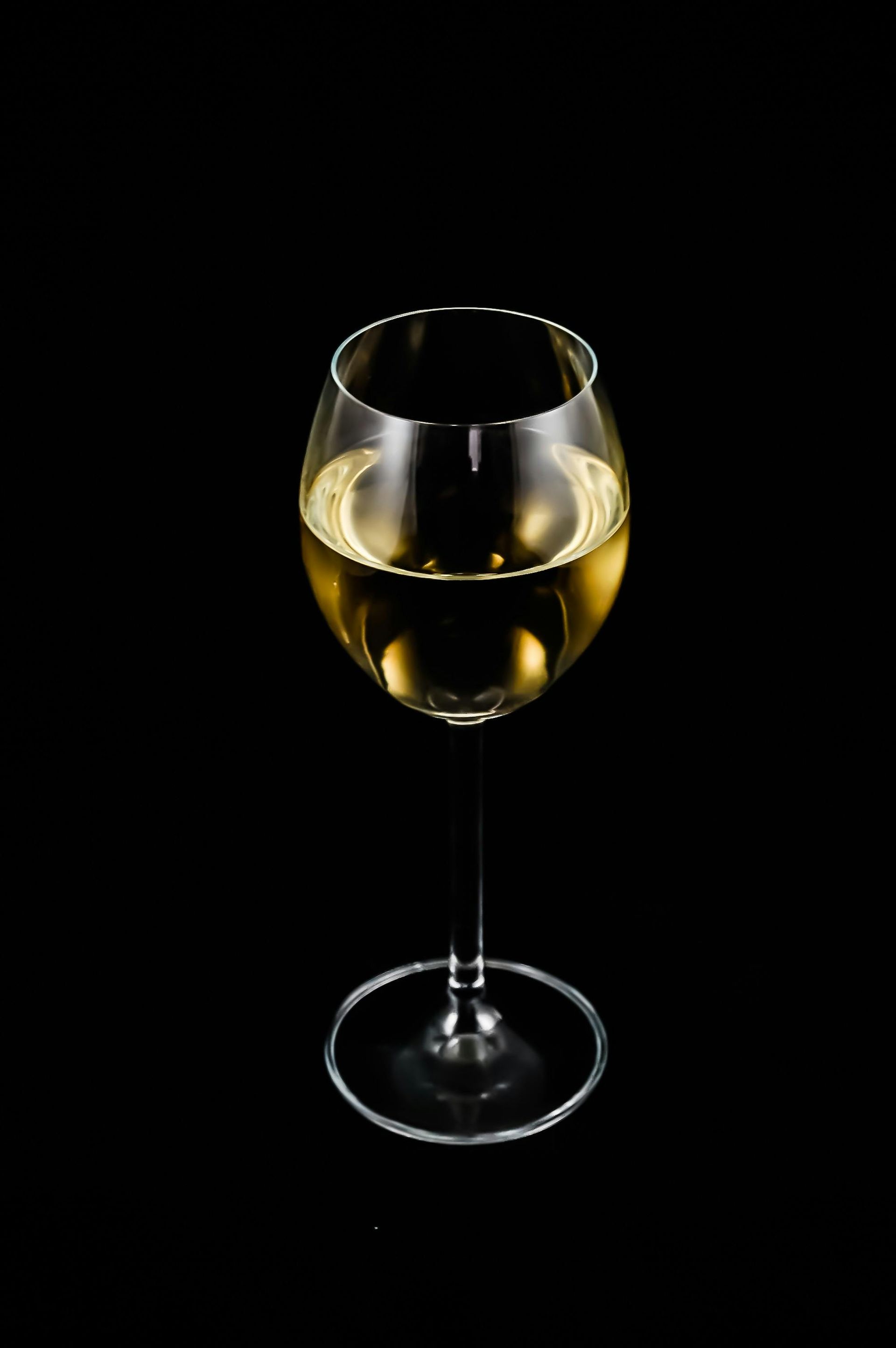 A glass of white wine on a black background.