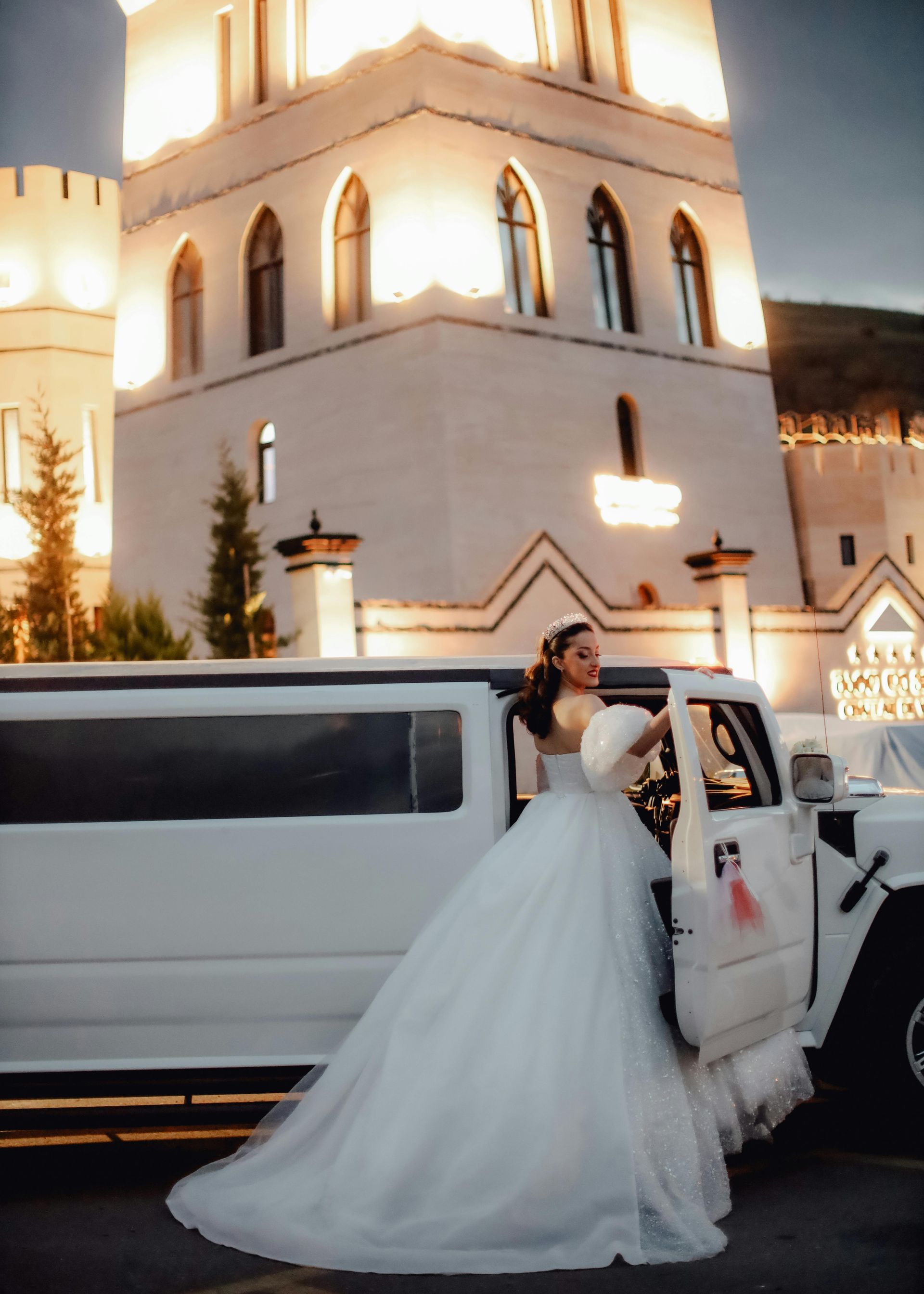 A bride in a wedding dress is getting out of a white limousine.