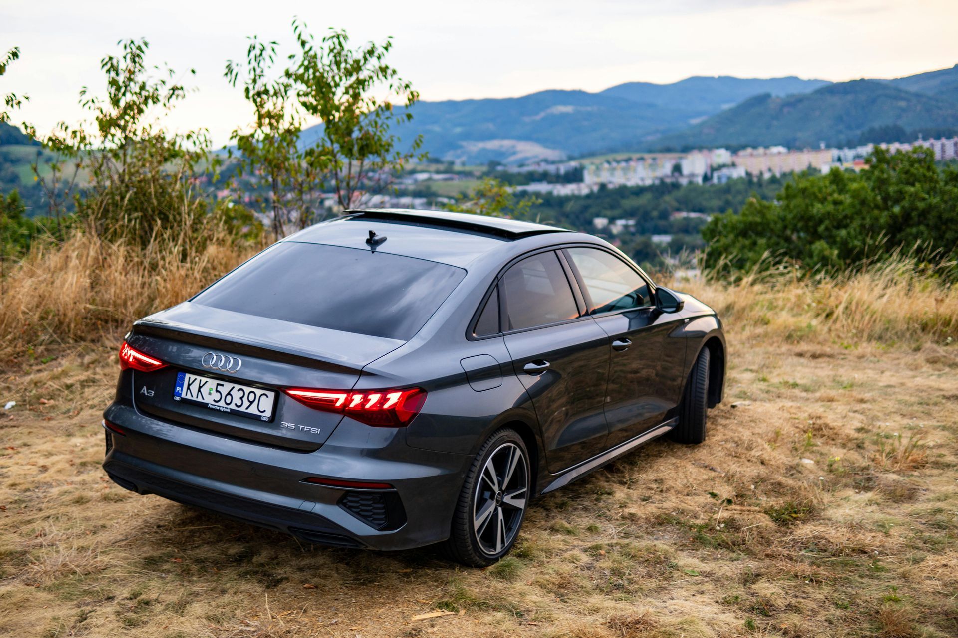 A black audi a3 is parked in a field with mountains in the background.