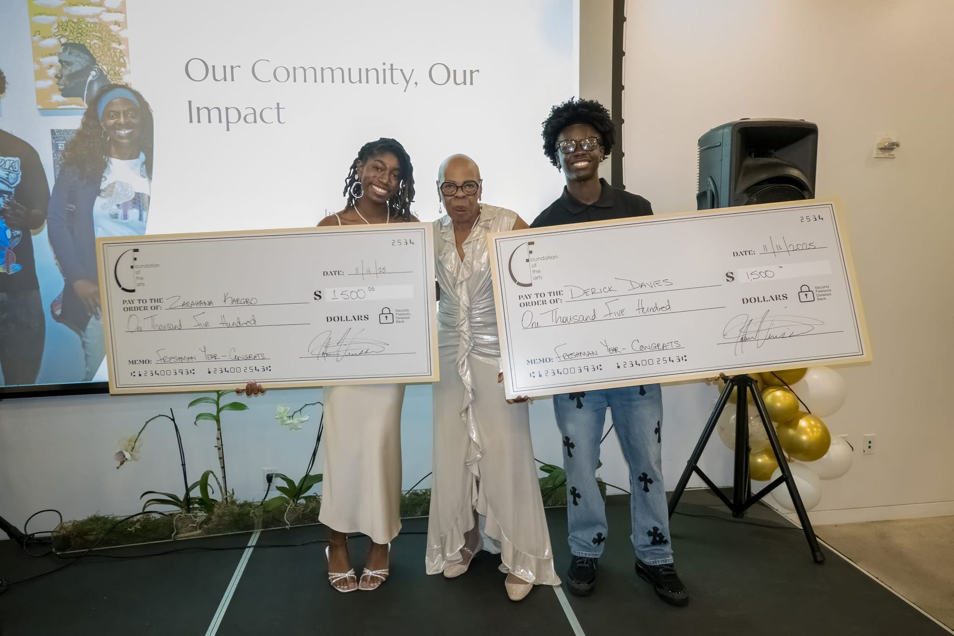 Three people holding oversized checks on stage; a presentation backdrop.