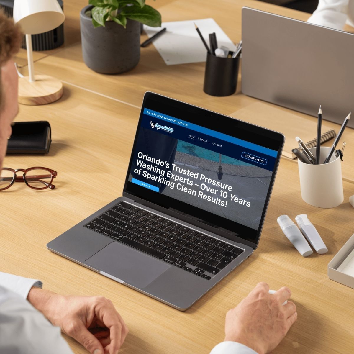 Person using a laptop at a desk, viewing a website for pressure washing services.