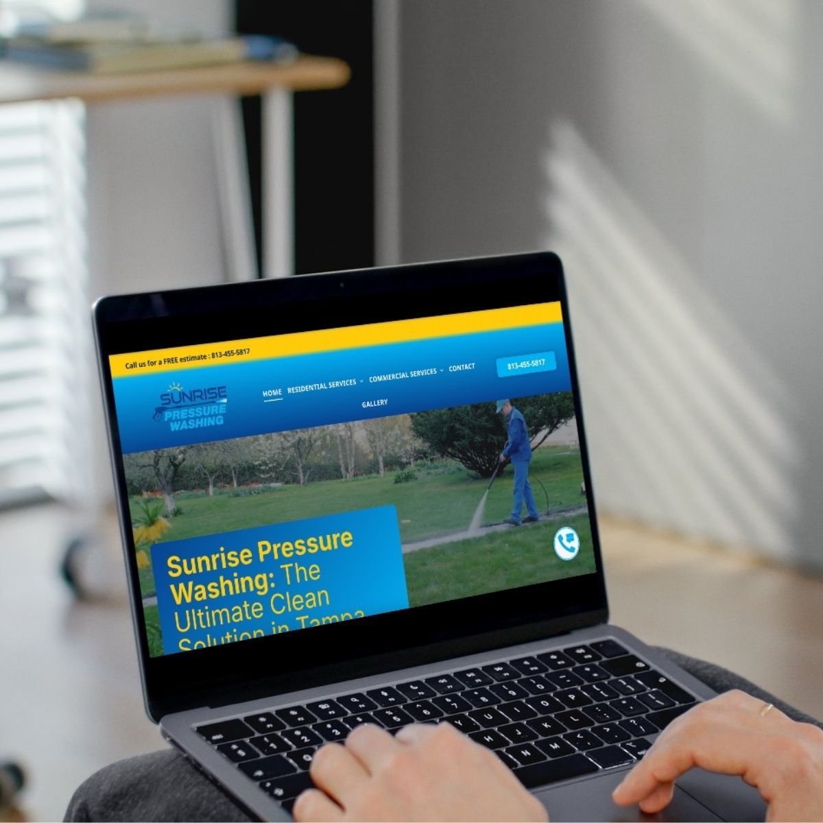 Person using laptop, viewing website for Sunrise Pressure Washing, featuring a man using a pressure washer on a lawn.