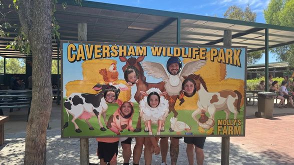 People posing with animal cutouts at Caversham Wildlife Park entrance sign.