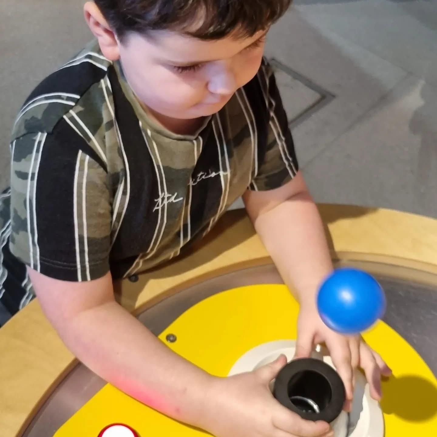 Boy focused on a blue ball levitating above a yellow table with a black cylindrical object.