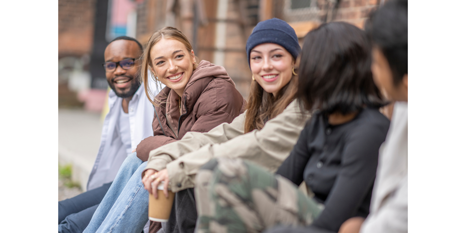 Group of diverse young adults smiling and sitting outside together.