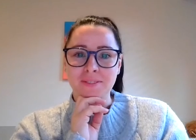 Woman with glasses, resting chin on hand, smiles. Blue sweater, light-colored background, abstract art.
