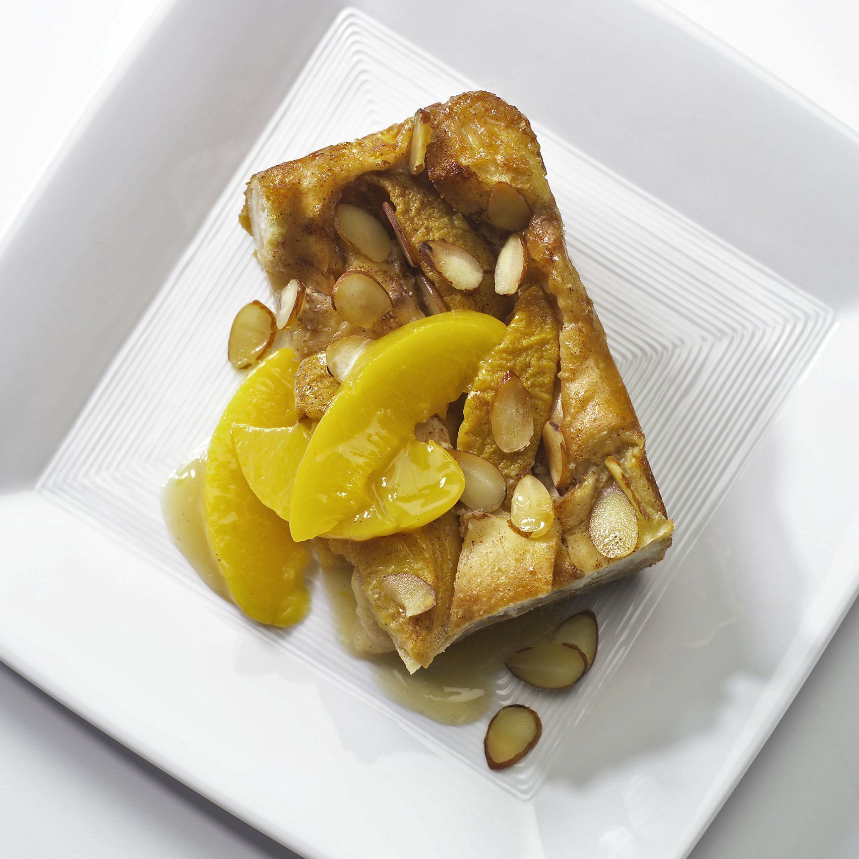 a piece of bread pudding with peaches and almonds on a white plate