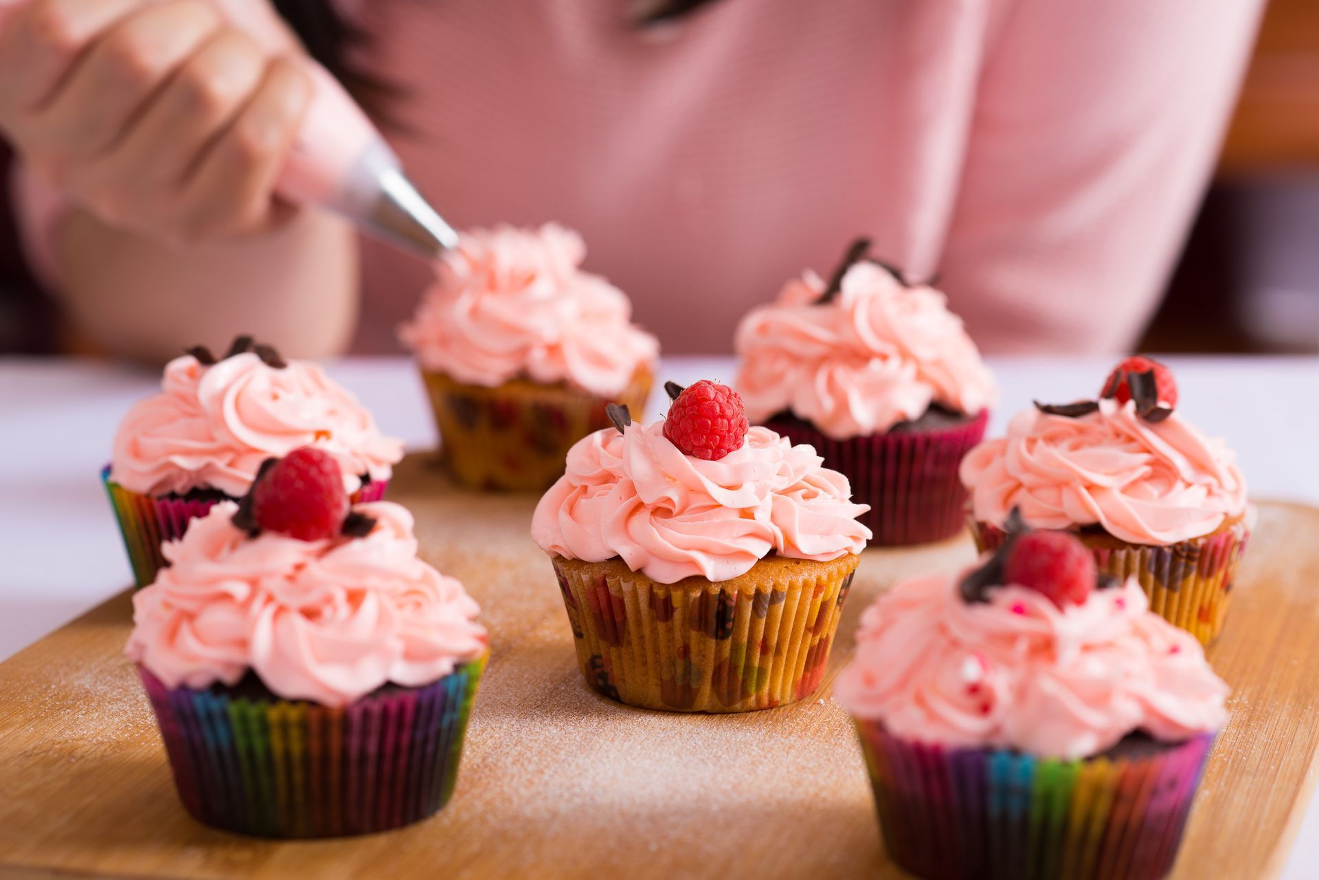 a woman decorates cupcakes with pink frosting and raspberries
