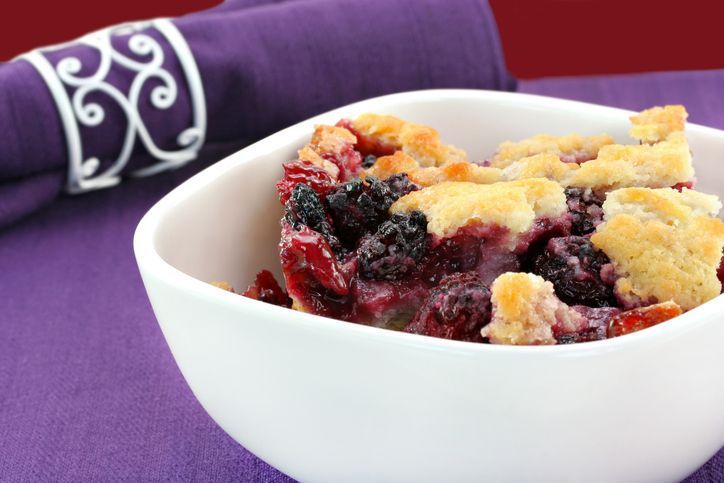 a bowl of berry cobbler sits on a purple table cloth
