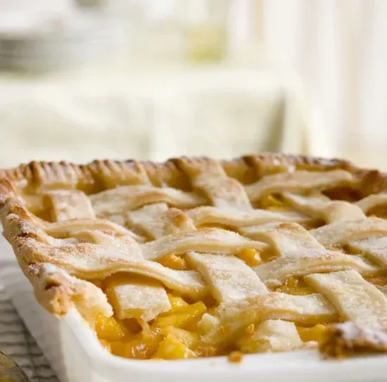 a close up of a peach pie in a white pan on a table .