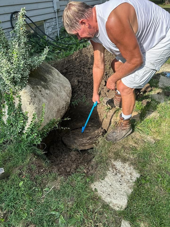 A man is digging a hole in the ground next to a large rock.