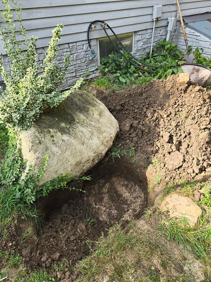 A large rock is sitting in the dirt in front of a house.