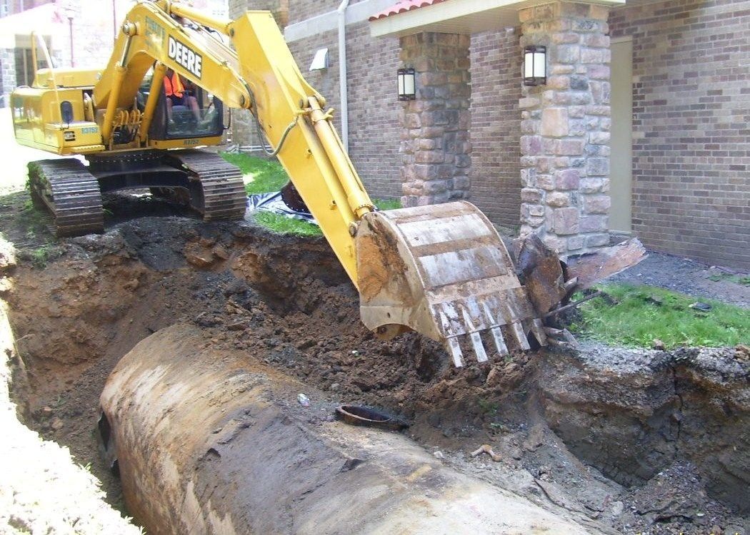 Yellow excavator digging near a building; revealing a large, buried metal tank.