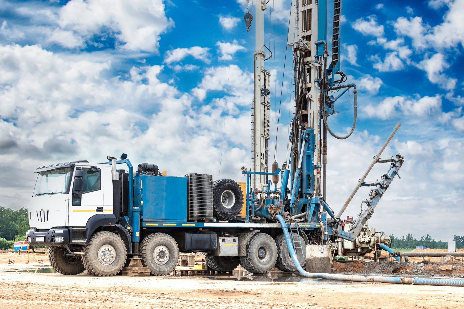 A large blue and white drilling rig on a truck, working outdoors under a cloudy sky.