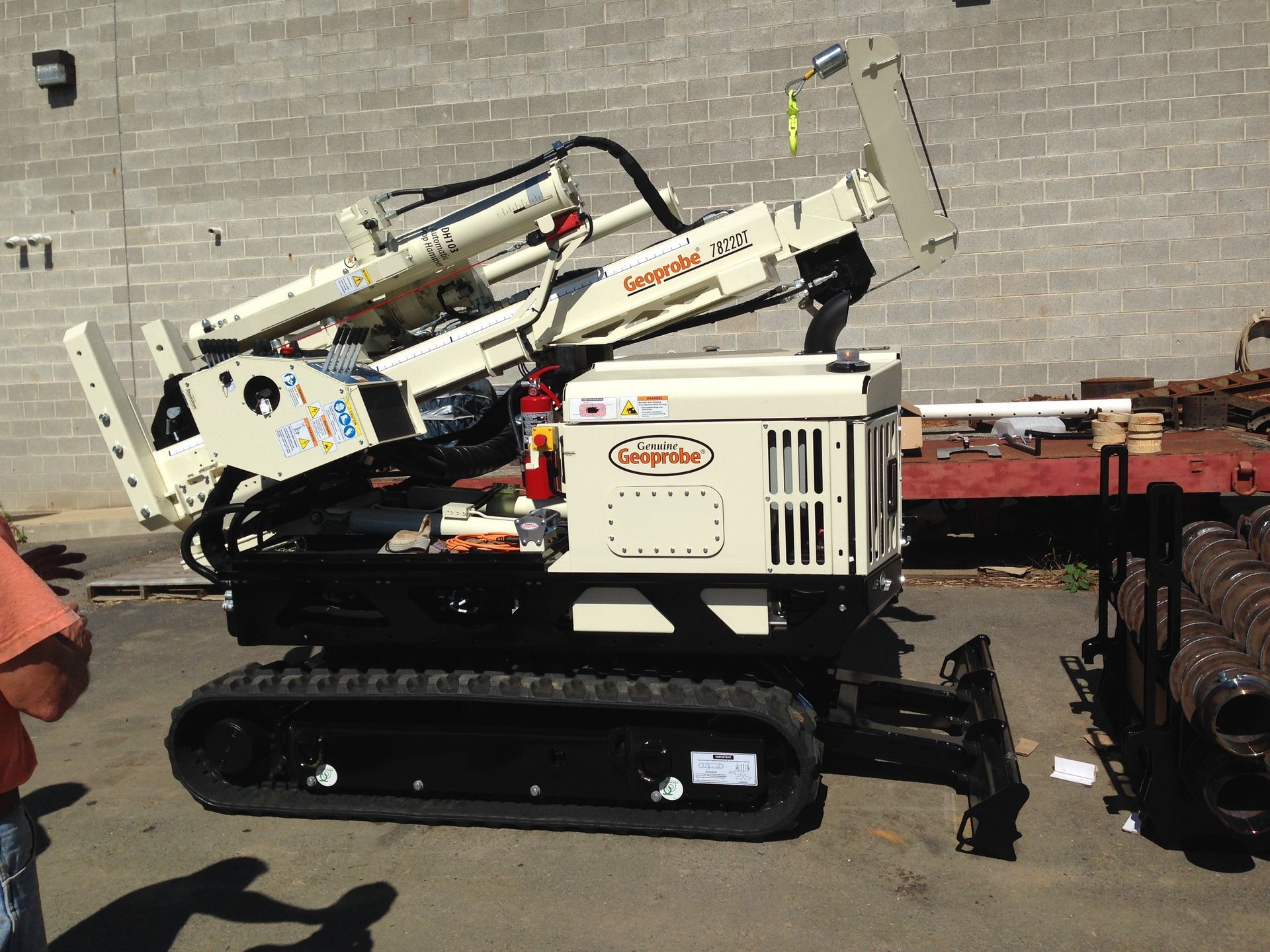 Cream-colored directional drilling machine on tracks, near a gray brick wall.