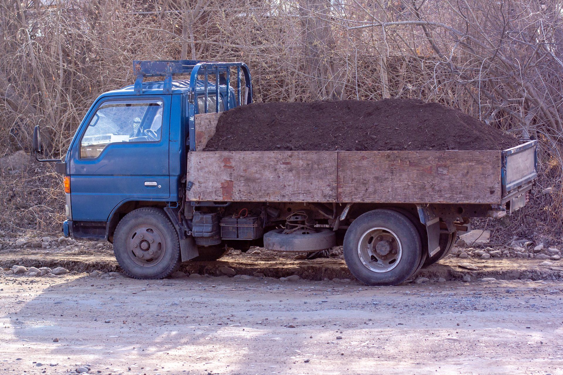 An aged pickup truck with a substantial mound of dirt in its cargo bed.