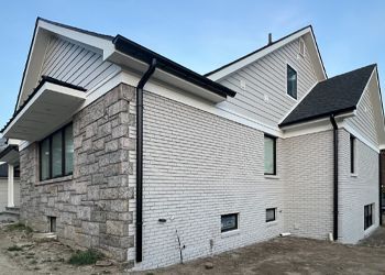 a white brick house with a black gutter on the side of it .