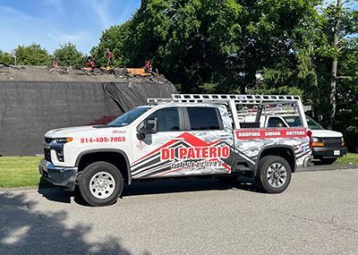 a white truck with a ladder on the back is parked on the side of the road .