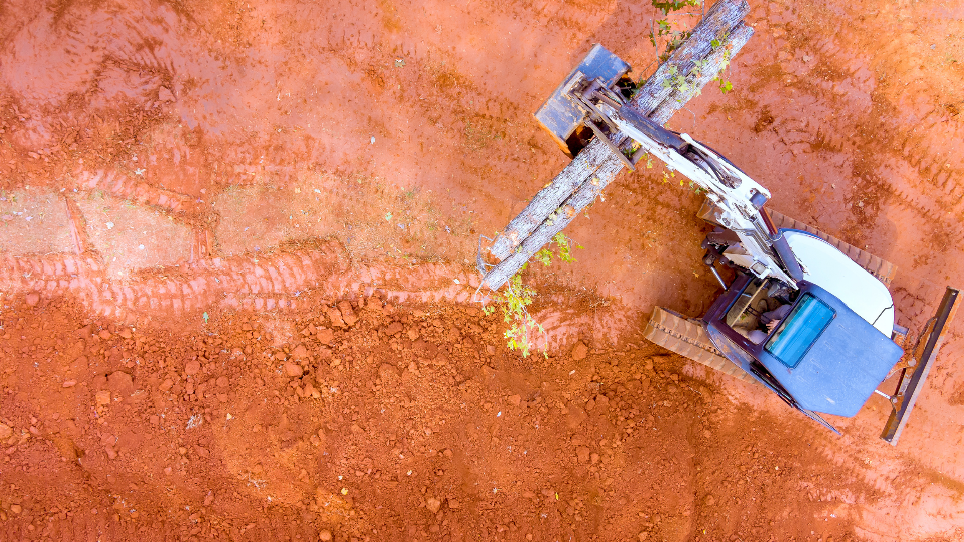 Aerial view of a blue excavator working on orange dirt at a construction site