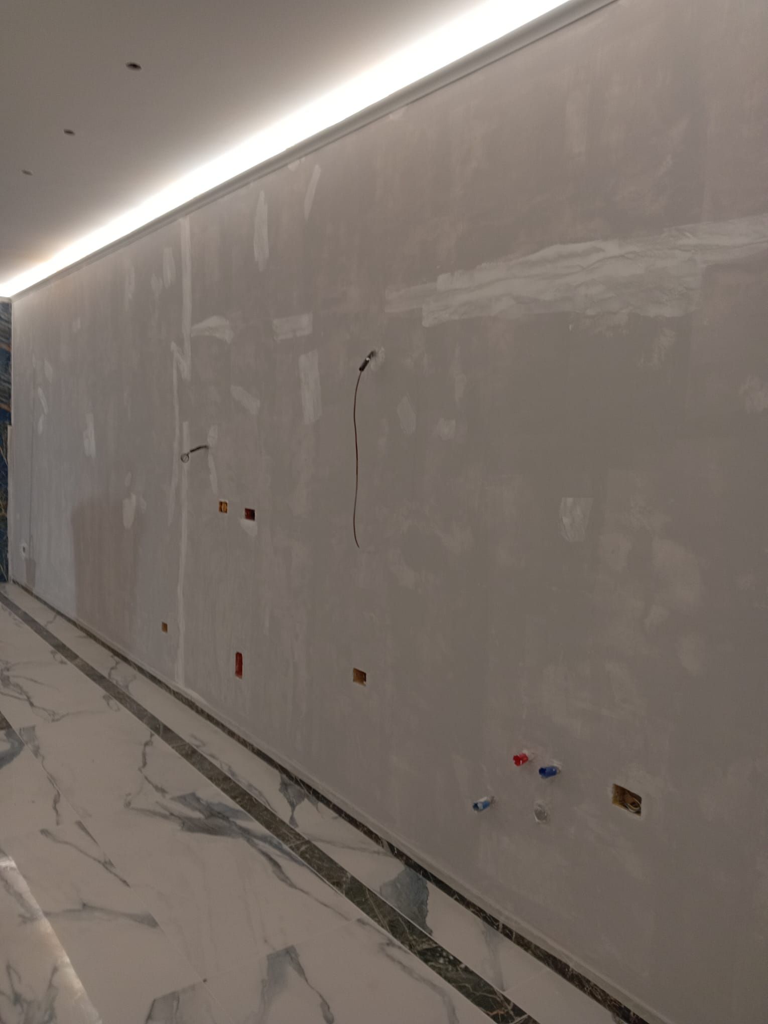 Un lungo corridoio con una grande parete bianca e un pavimento in marmo.