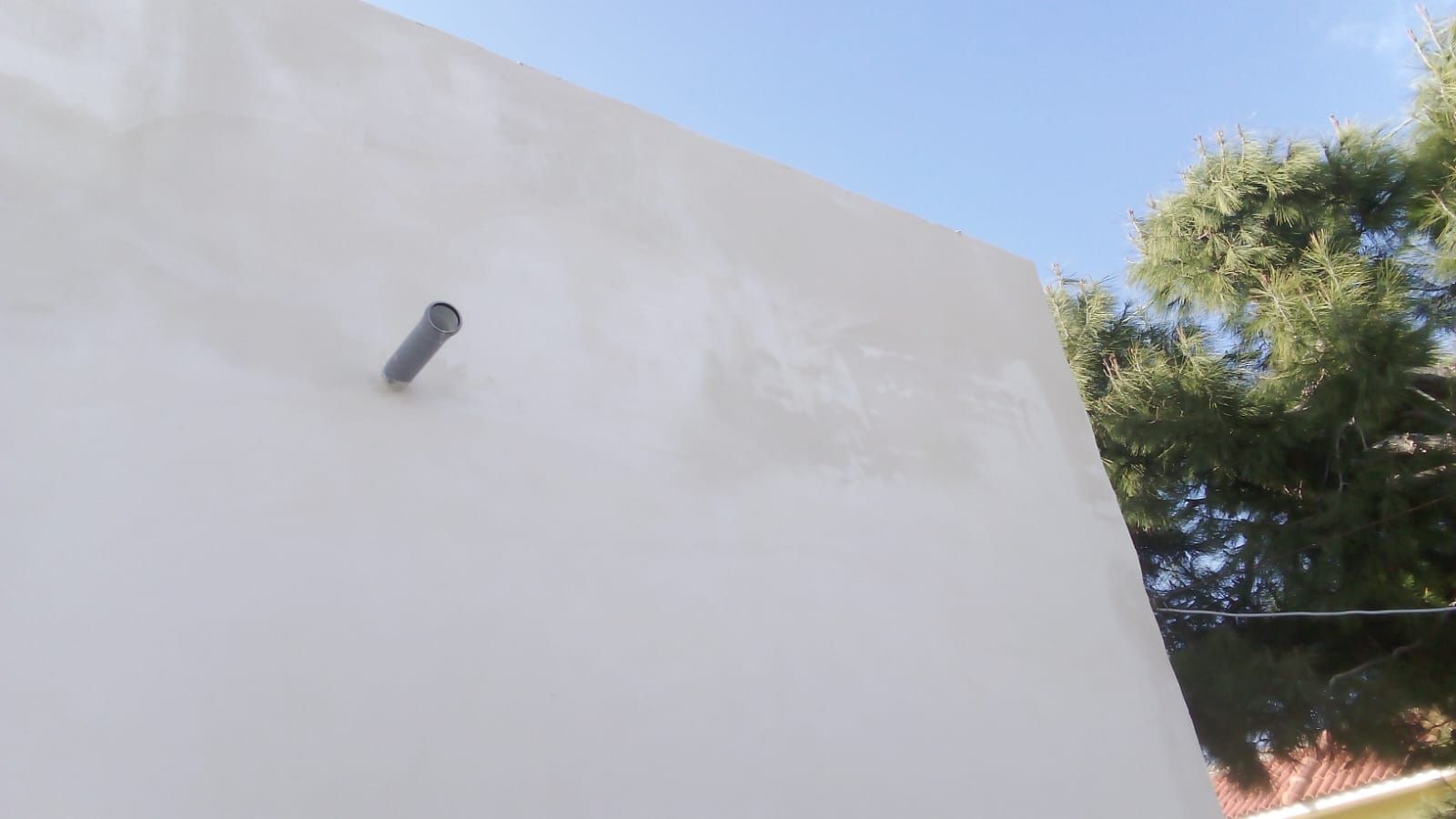 Un muro bianco da cui spunta un tubo.