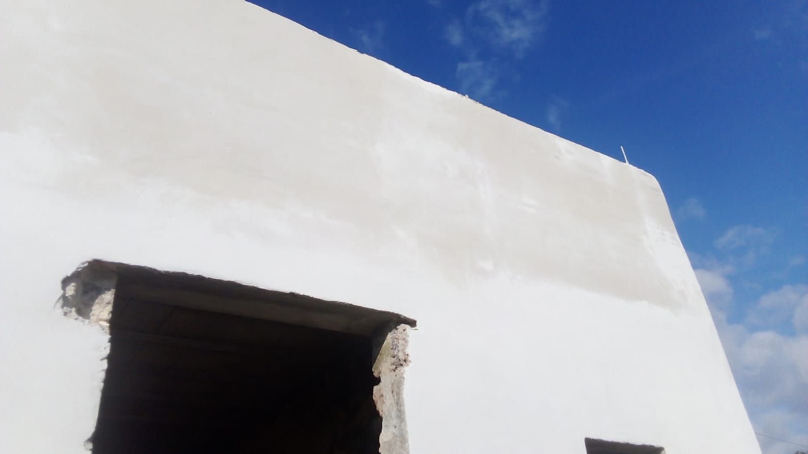 Un edificio bianco con una porta nera e un cielo blu sullo sfondo.