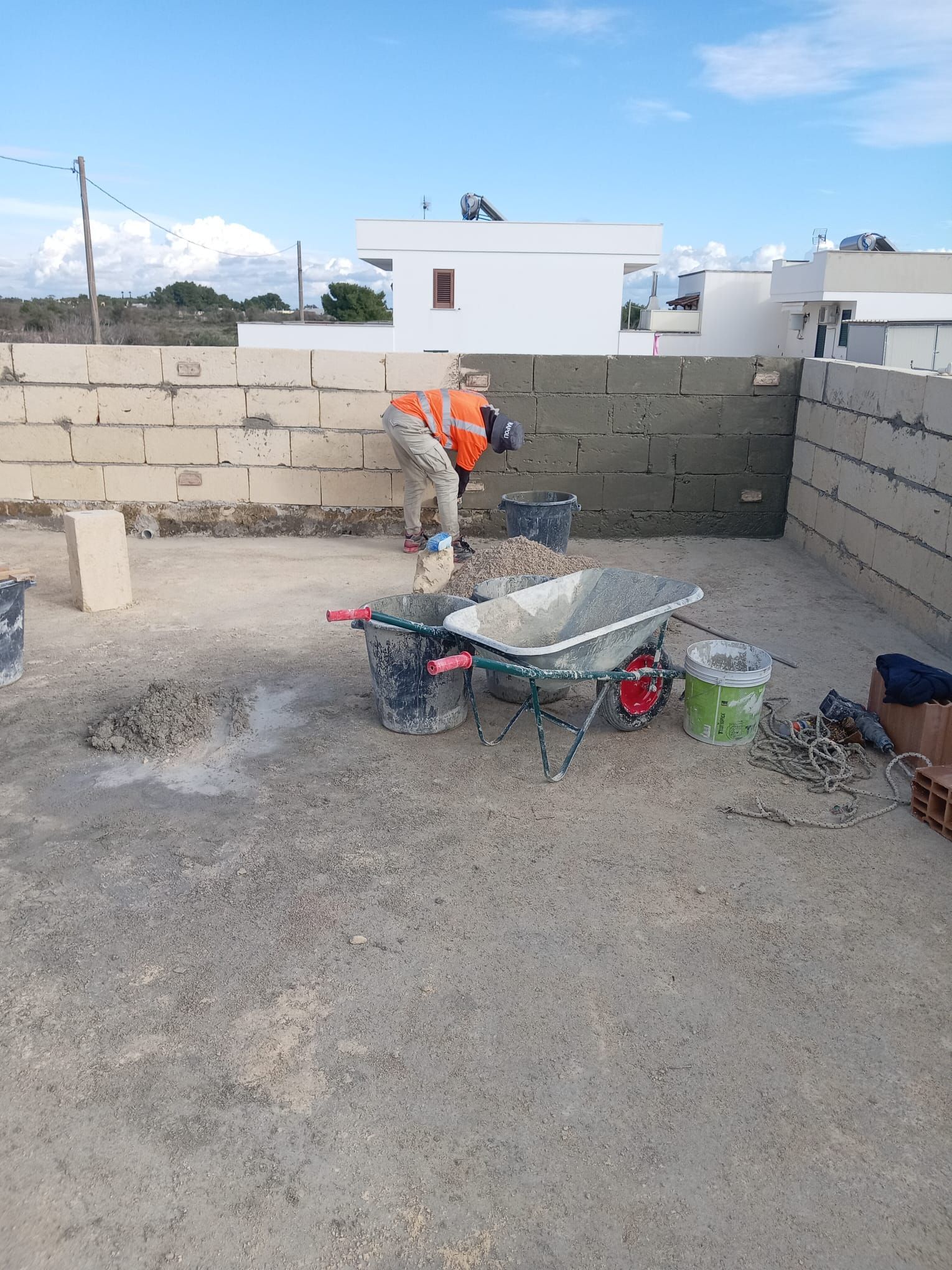 Un uomo sta lavorando su un muro accanto a una carriola.