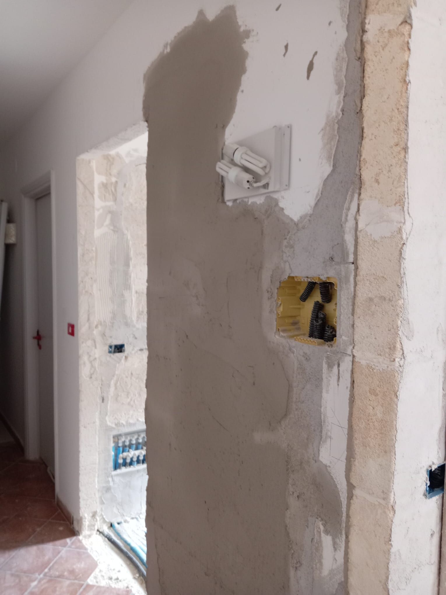 Un corridoio con una porta e un muro con un buco.