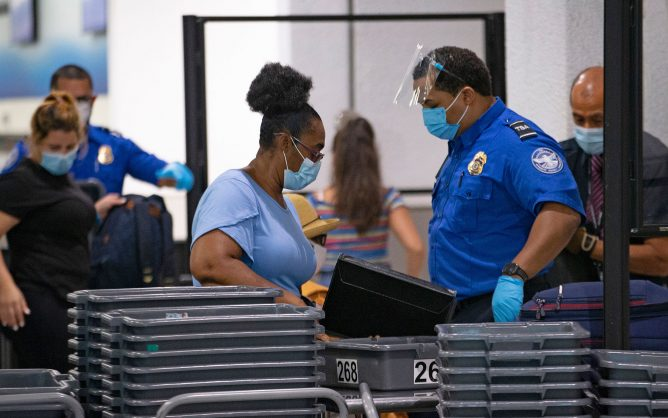 A TSA worker wears a mask while helping travelers get through a security checkpoint at Miami International Airport. (David Santiago/Miami Herald/TNS)