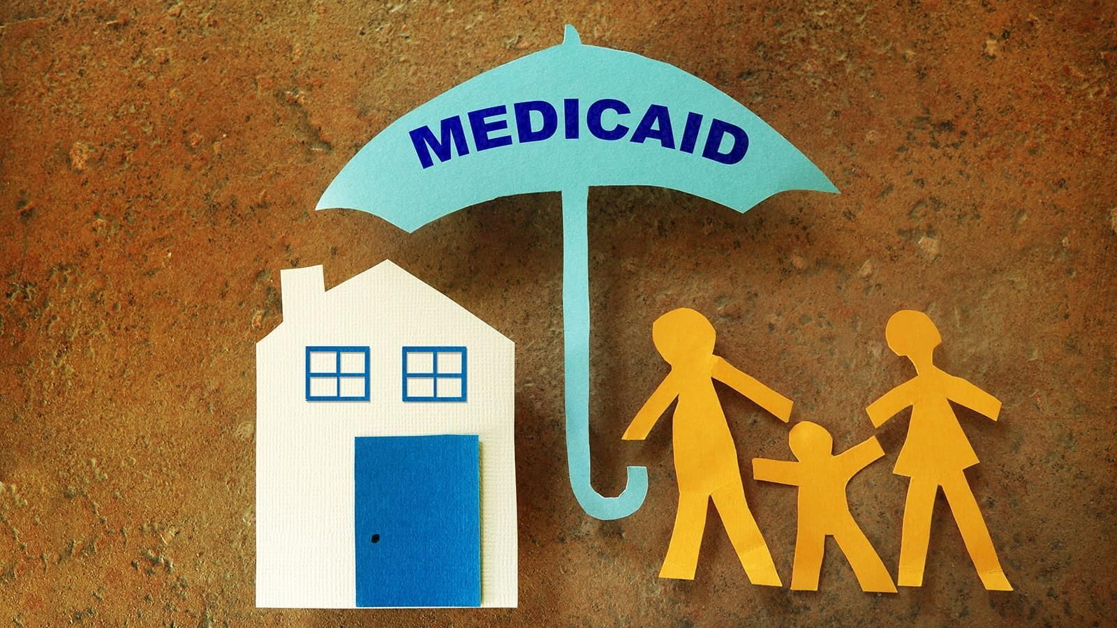 Paper cut outs of a home and family of three under a Medicaid umbrella.