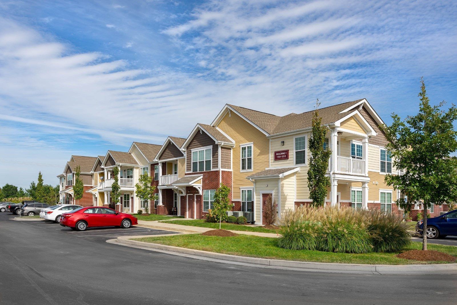 A row of apartment buildings with cars parked in front of them.