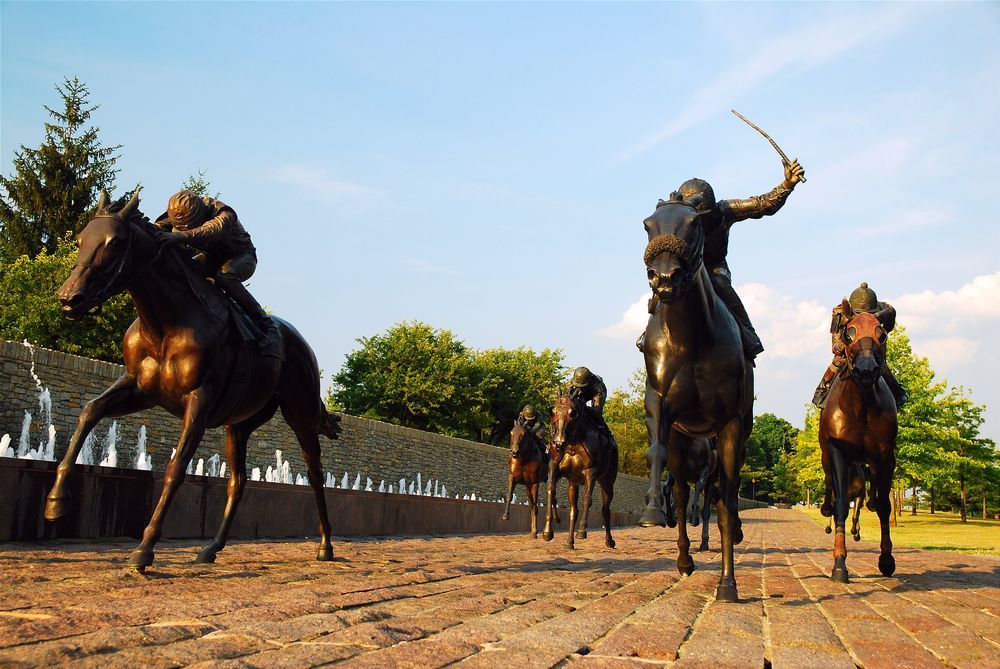 A group of statues of people riding horses on a cobblestone road