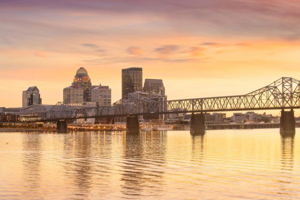 A bridge over a body of water with a city skyline in the background at sunset.