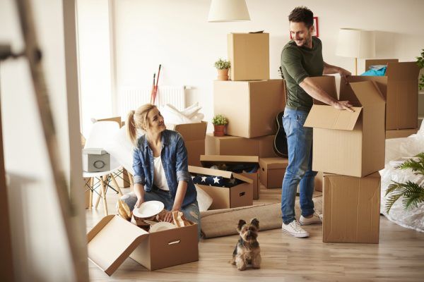 A man and woman are moving into a new house with a dog.