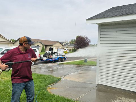 A man is using a high pressure washer to clean a sidewalk in front of a house.