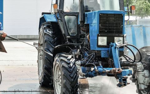 A man is washing a blue tractor with a high pressure washer.